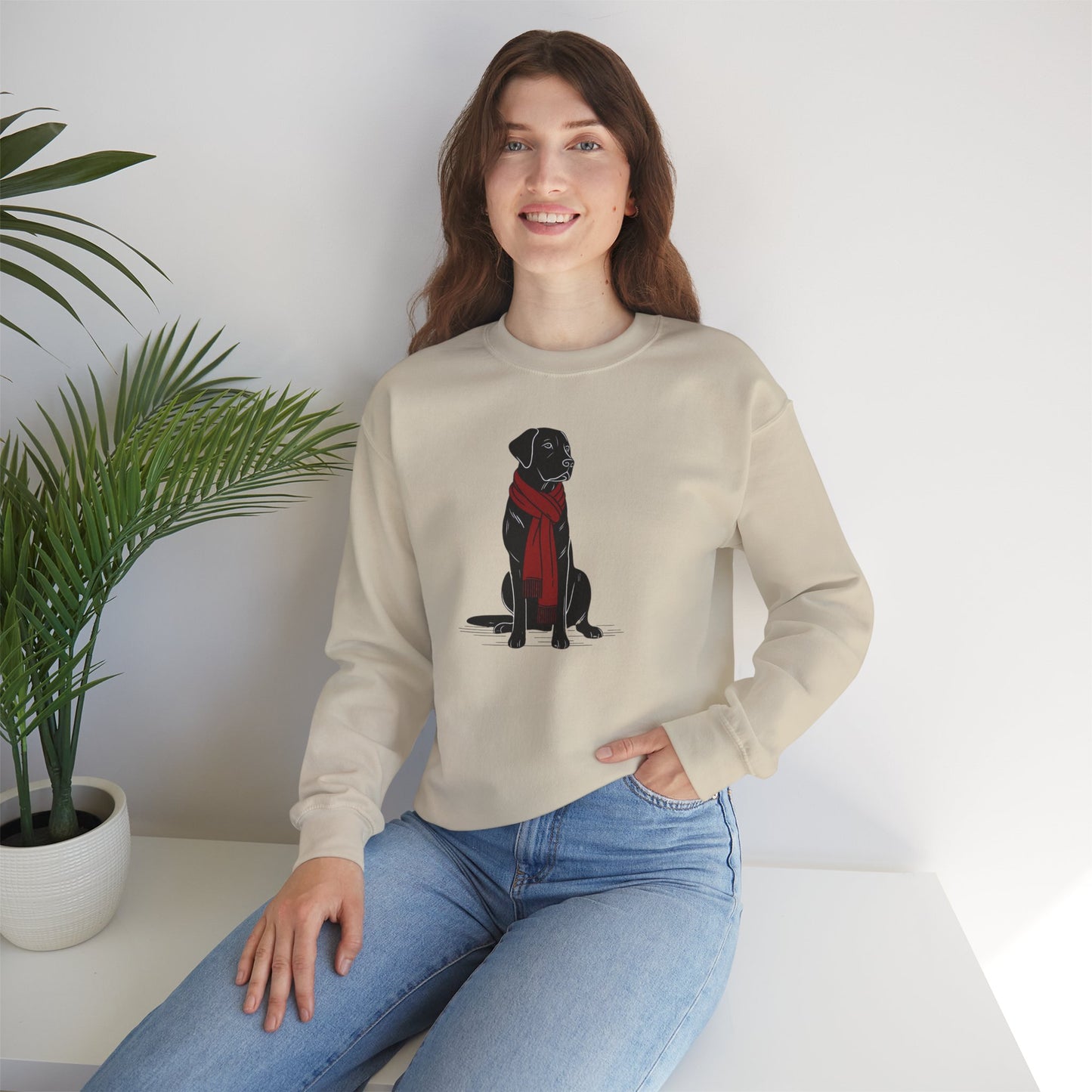 Woman wearing a beige sweater with a dog design, sitting in a room with a plant.