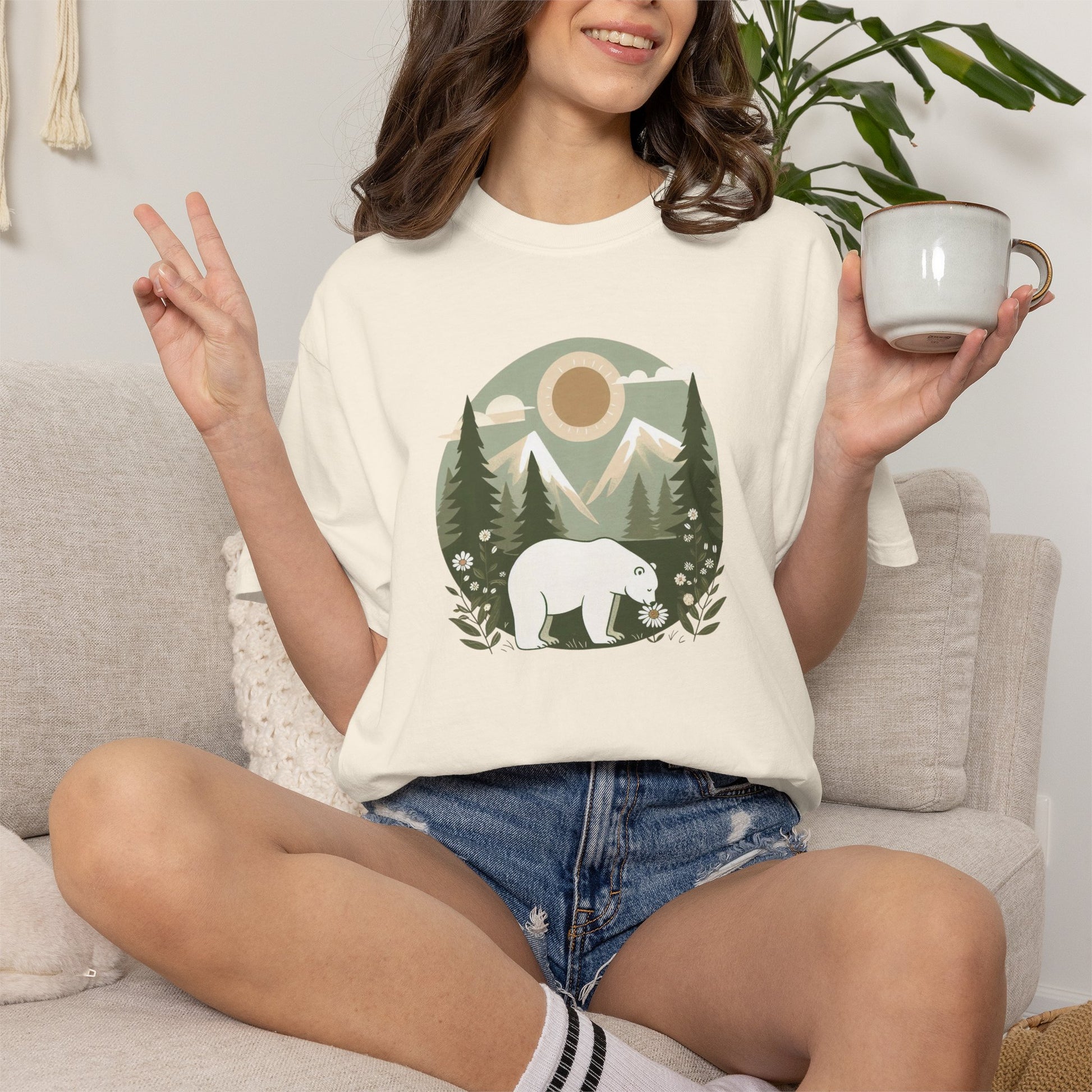 Person wearing a white t-shirt with a bear graphic, sitting on a couch holding a mug.