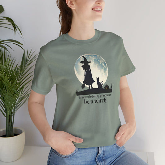 Empowering feminist green t-shirt with illustrated witch under the moon, with a cat and pumpkin. In a world full of princesses be a witch