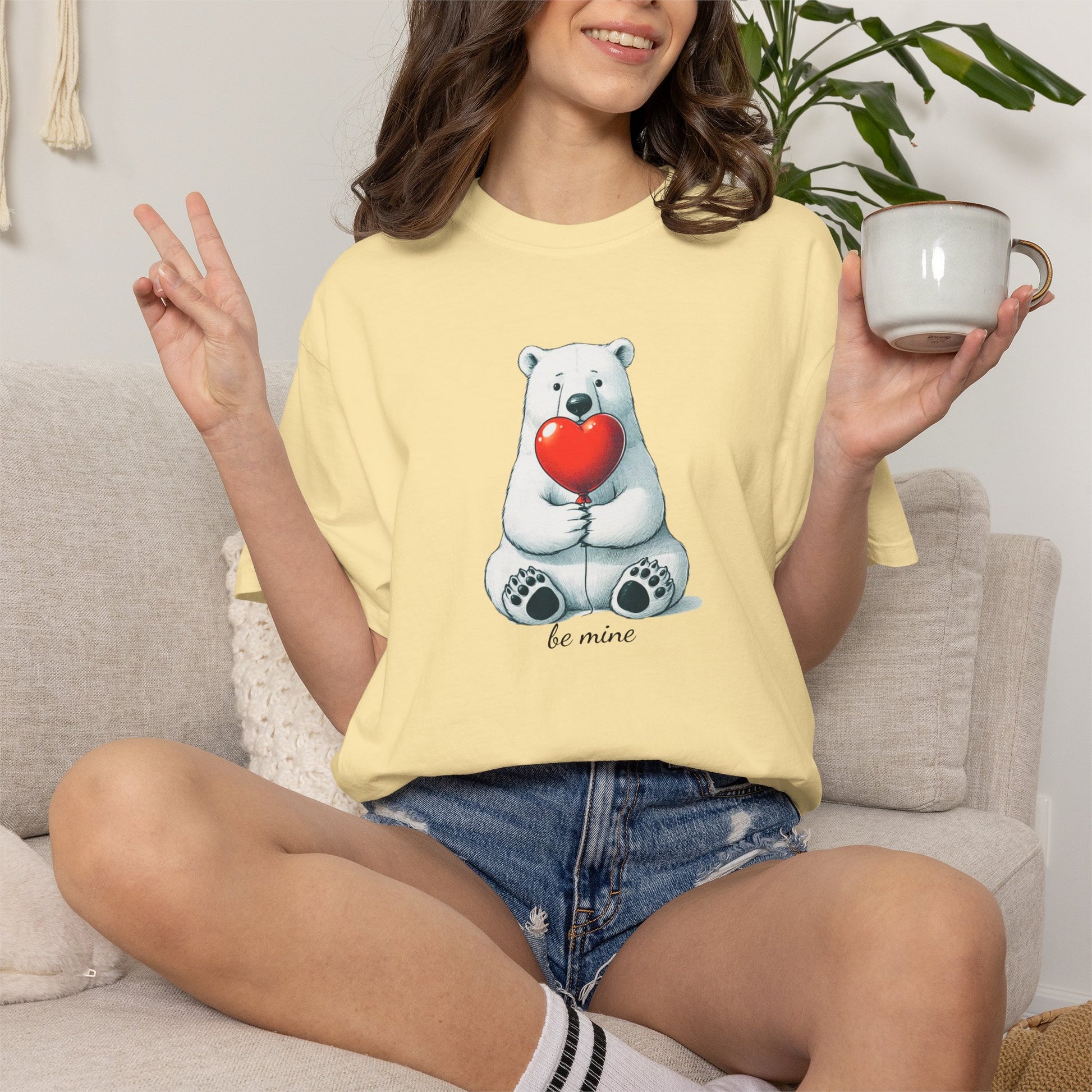 Person wearing a yellow t-shirt with a bear holding a heart design, sitting on a couch.