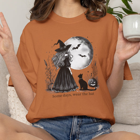 Person wearing a Halloween-themed orange t-shirt with a witch design, sitting on a couch holding a mug.