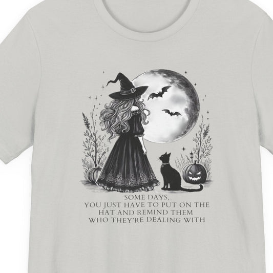 White t-shirt with text and a witch with a moon and cat graphic on a background