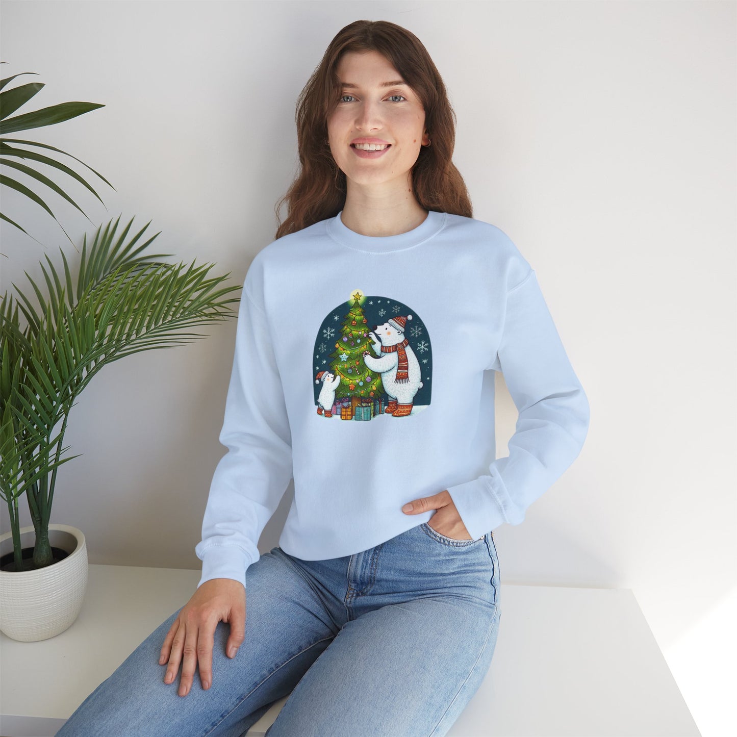 Woman wearing a light blue sweater with a Christmas design, sitting on a white surface with a plant in the background.