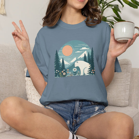 Person wearing a blue t-shirt with a nature graphic, sitting on a couch holding a mug.